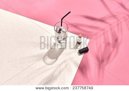 High Angle View Of Lipstick And Drinking Glass With Ice On Table. Pink And White Background With Sha