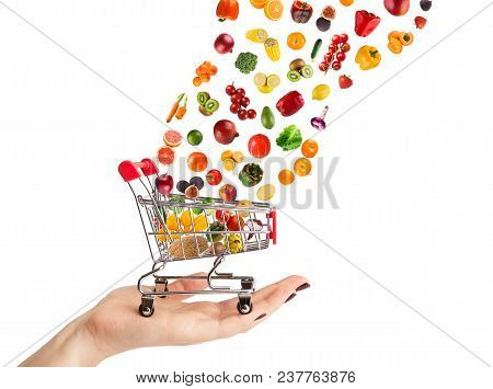 Female Hand Holding Grocery Cart With Vegetables And Fruits Falling In It Isolated On White. Healthy