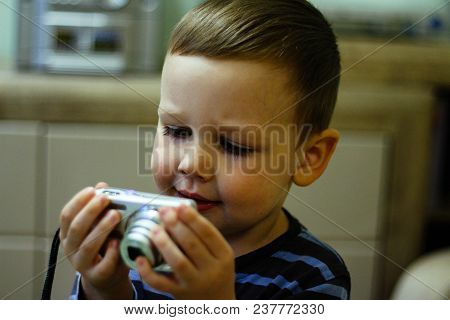 A Small Boy Holds A Camera In His Hands And Stares At The Screen With Comprehension. Memories, Pictu