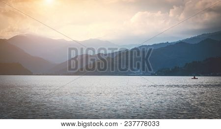 View on Phewa lake surrounded by mountains in light fog in the evening, Pokhara, Nepal.