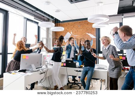 Young Multi-ethnic Group Of Office Workers Are Celebrating Triumph. Flying Paper. Throw Documents