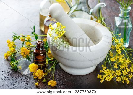 Mortar With Fresh Wild Flowers And Essential Oil In Glass Bottles