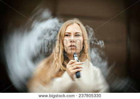 Vape Teenager. A Young Cute White Girl Is Vaping An Electronic Cigarette On The Street In Sping.