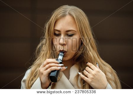 Vape Teenager. A Young Cute White Girl Is Vaping An Electronic Cigarette On The Street In Sping.