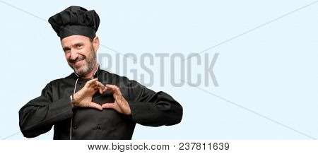 Senior cook man, wearing chef hat happy showing love with hands in heart shape expressing healthy and marriage symbol isolated over blue background