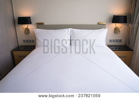 Small Bedding Area In Hotel Room. Double Bed Near To Window Complemented With Two Lamps And Cabinets
