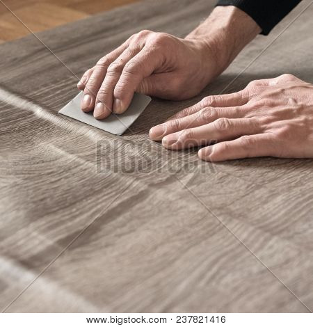 Closeup Of Carpenters Hands Removing Air From Self-adhesive Film