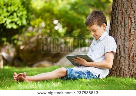 Child with tablet pc outdoors. Boy on grass with computer
