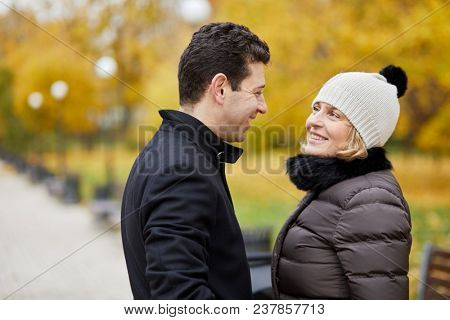 Half-length portrait of smiling man and woman in autumn park, profile view.