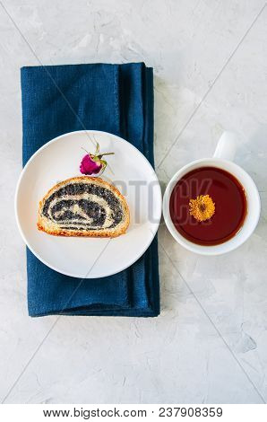 Slice Of Poppy Seed Roll Served On A Plate And A Cup Of Flower Tea On A White Stone Background.
