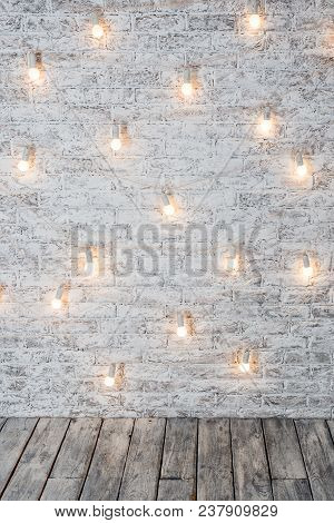 Light Bulbs On White Brick Background With Wooden Floor. Vintage Edison Light Bulbs Garland In Loft 