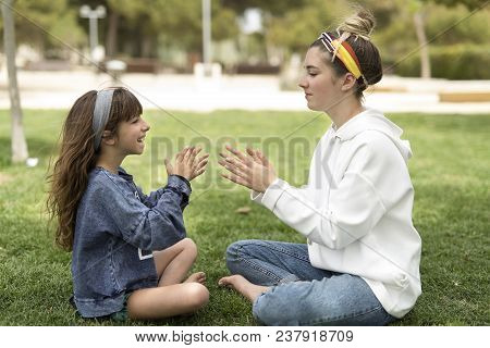Two Sisters Playing In A Park Sitting On The Grass.