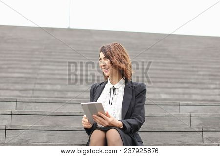 Smiling Businesswoman Sitting On Stairs With Laptop. Concept Of Working In Open Ait And Modern Techn