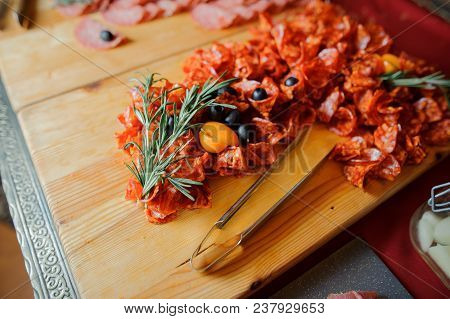 Cutted Wurst On The Wooden Plate Decoreted With Black Olives, Little Yellow Tomatoes And Rosemary Br