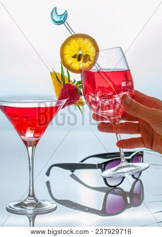 Women Hand Holding One Of Cocktail Glasses Decprated With Tropicl Afruits And Leaves On A Reflective