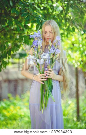 Attractive Young Girl With Blonde Dren Hair And Natural Make-up Smelling Blue Purple Iris Flowers On