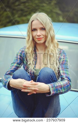 Cheerful Attractive  Young Blonde Girl  Posing On The Hood Of An Old Rusty Car, Dressed In Jeans And