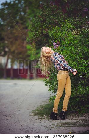 Pretty Woman Blonde On A Rustic Road Is Happy, Against A Background Of Lots Of Green Trees, A Beauti