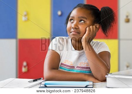 Close Up Portrait Of Little African Female Student Sitting At Desk In Classroom. Tedious Kid With Bo