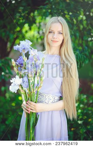 Attractive Young Girl With Blonde Dren Hair And Natural Make-up Smelling Blue Purple Iris Flowers On