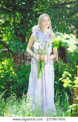 Attractive Young Girl With Blonde Dren Hair And Natural Make-up Smelling Blue Purple Iris Flowers On