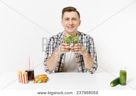 Man Sits At Table With Green Detox Smoothies, Salad In Glass Bowl, Cucumber, Burger, Fries, Cola In