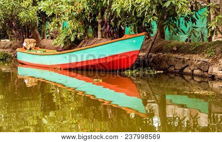 Small Boat Sits In Water Under Trees With Reflections In Water