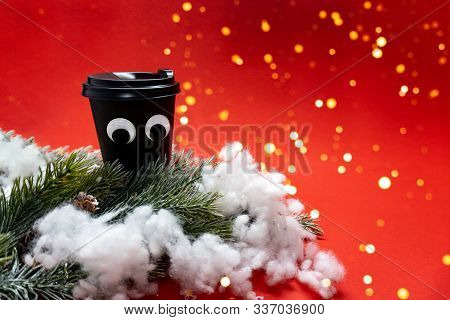 Black Coffee Cup With Plastic Cap And Googly Eyes Among Green Braches With Knar And Snow On Red Back