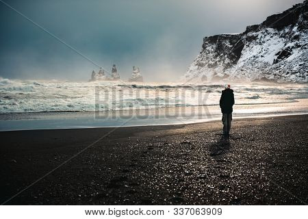 Traveler, woman standing on the black volcanic beach and enjoying amazing view on basalt sea stacks, Reynisdrangar in Atlantic ocean near Vik Myrdal, Iceland