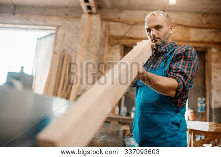 Carpenter with board near plane machine, carpentry