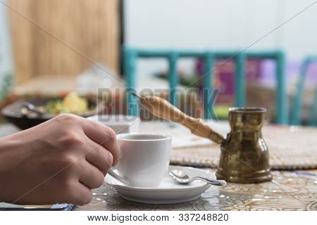 A Girl Holds A White Coffee Cup In Her Hand. Against The Backdrop Of An Arab Copper Coffee Pot