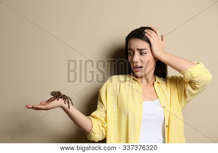 Scared Young Woman Holding Tarantula On Beige Background. Arachnophobia (fear Of Spiders)