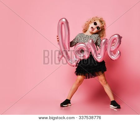 Blonde Kid Girl With Curly Hair In Leopard Print Shirt, Black Fatin Skirt And Sunglasses Is Posing W