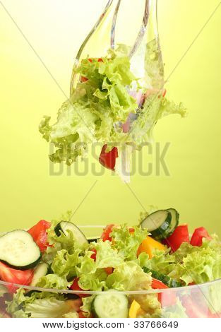 Frischer Gemüsesalat in transparente Schale mit Löffel und Gabel auf grünem Hintergrund