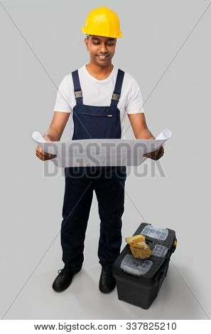 profession, construction and building - happy smiling indian builder in helmet with blueprint and tool box over grey background