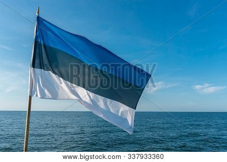 Flag Of Estonia On Blue Sky Background Flying In Strong Breeze Over The Baltic Sea. Estonian Nationa