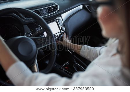 Pushing The Buttons. Beautiful Blonde Girl Sitting In The New Car With Modern Black Interior.