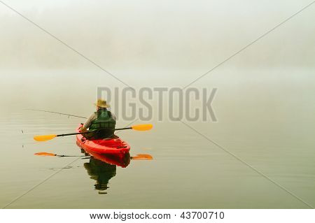 pescatore in kayak rosso, mattina nebbiosa