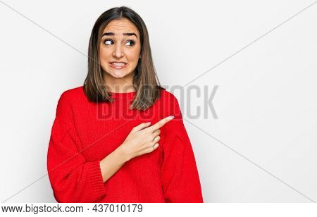 Beautiful brunette woman wearing casual winter sweater pointing aside worried and nervous with forefinger, concerned and surprised expression 