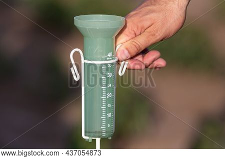 Close Up Of Farmer's Hand Holding Rain Gauge In Field. Measuring Watering Field After Rainfall