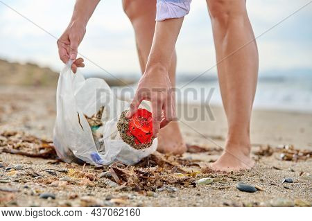 Close-up Of A Womans Hands Picking Up Plastic Trash Into A Bag On The Beach