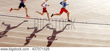 Group Runners Run Middle Distance In Stadium. Shadows Of Silhouettes On Track