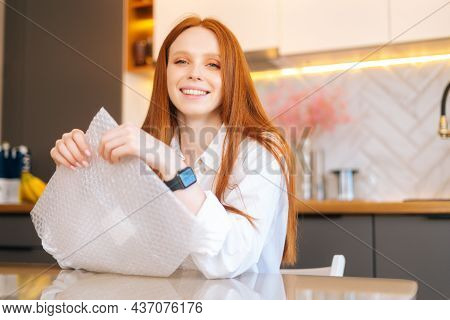 Close-up Portrait Of Happy Young Woman Playing Pops Bubble Wrap To Calm Herself Sitting At Table In 