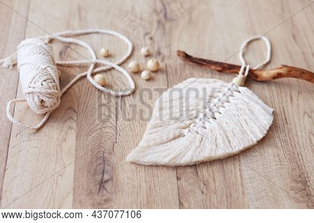 Macrame Leaf  In Natural Color And Thread Windings Lying On A Wooden Table. Cotton Rope Decor Macram