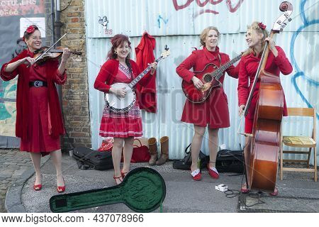 London, Uk - 20 November 2019, A Group Of Girls In Red Robes Play Instruments And Sing At The Flower