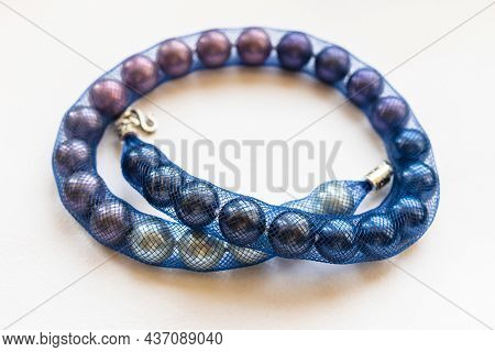Artificial Pearl Necklace In Blue Jewelry Mesh Close Up On White Paper
