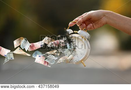 Woman Holding Crumbling Alarm Clock With Flying Euro Banknotes Outdoors