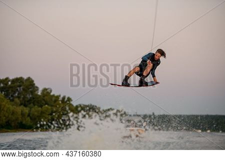 Energy Man Flying Over Splashing Wave On Wakeboard Holding On To The Rope