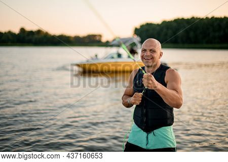 Selective Focus On Smiling Man In Vest Pulling Rope Against Water Background