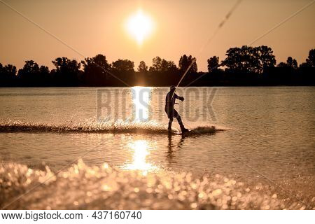 View Of Male Wakeboarder Riding Water Against Bright Sunset Background